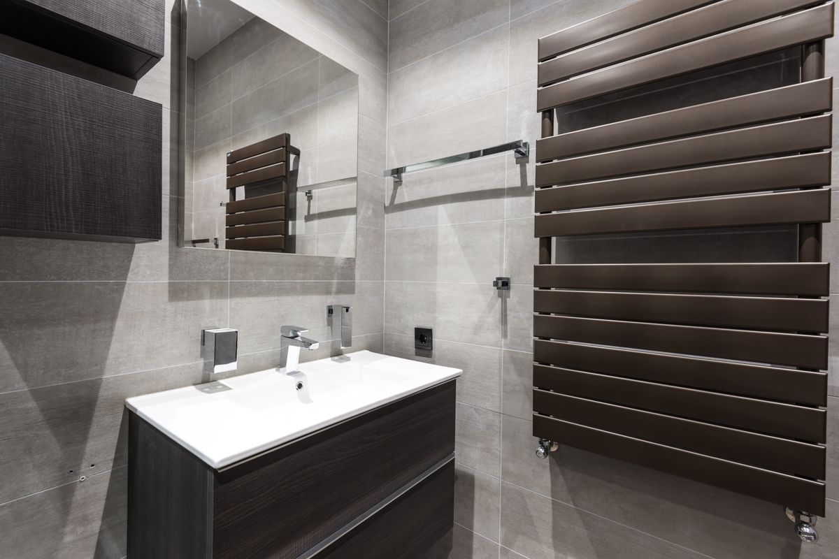 Wall-mounted basin and dark cabinetry against grey bathroom tiles