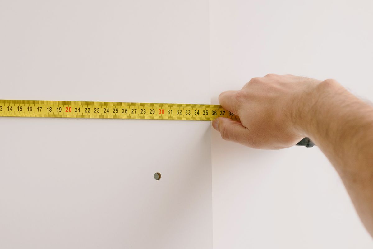 A hand holding a tape measure against a wall