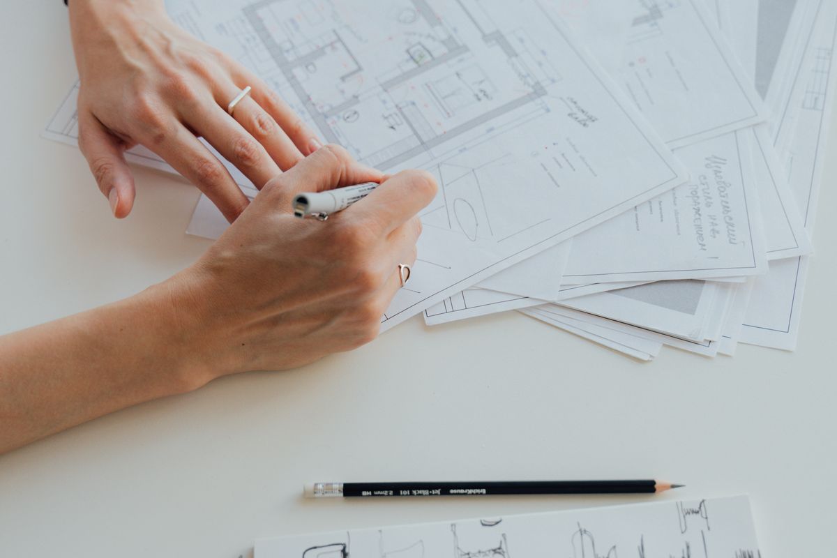 Hands drawing a floor plan with drafting tools on a desk