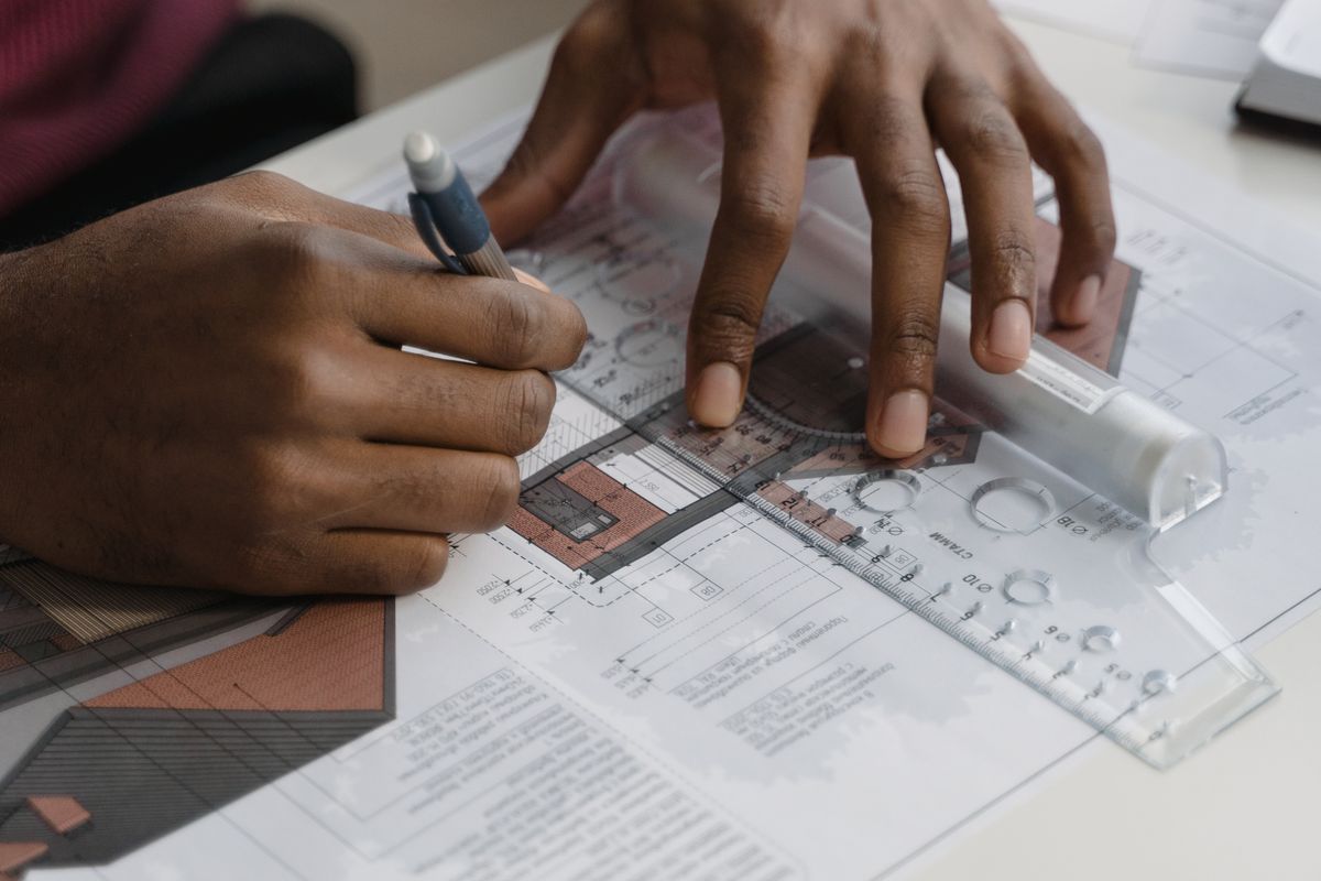 Hands drawing a building plan using a ruler and pencil