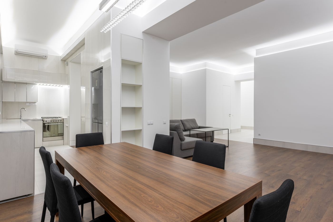 Wooden dining table beside kitchen cabinetry, shelving and a shared living area